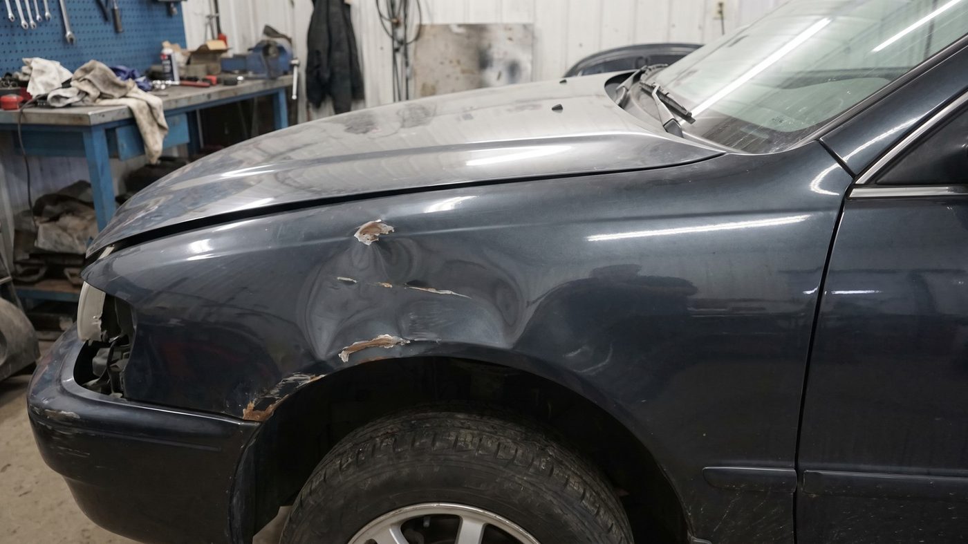 Fahrzeug-Kotflügel mit Delle und Lackschaden vor der Reparatur
